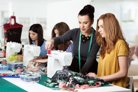 An instructor demonstrates sewing techniques to students in a fashion design classroom.