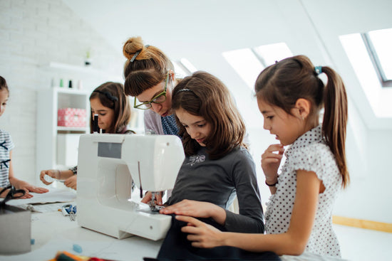 An instructor guides young students in a beginner class as they learn to sew with a sewing machine.